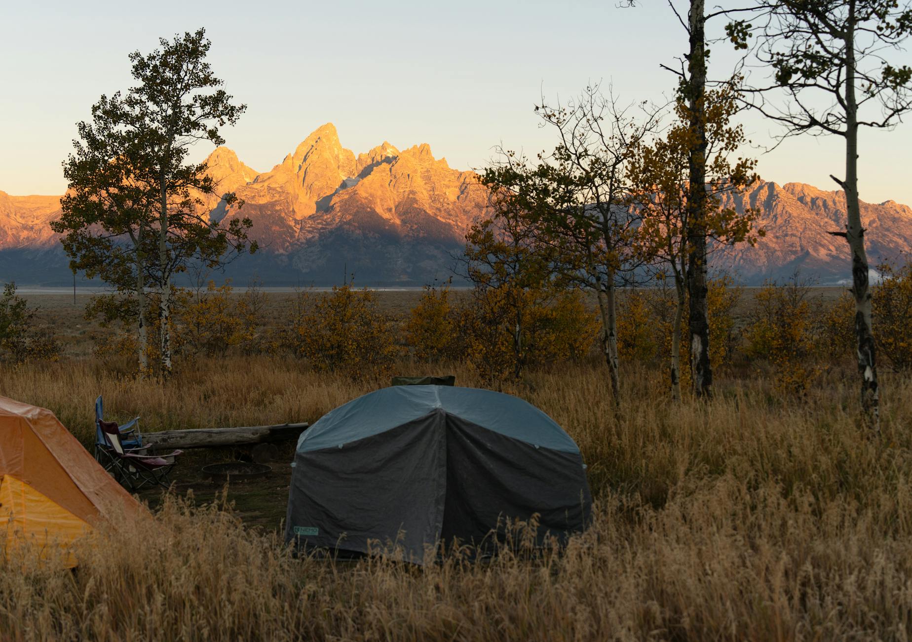 Tent hunting camp at first light with sharp Teton-like peaks behind golden fall aspens